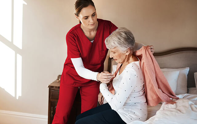 Female PSW assisting senior female patient with getting dressed